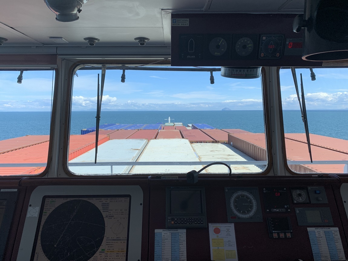 Cargo ship bridge overlooking a loaded container deck, showing the operational complexity of freight coordination across supply chains.