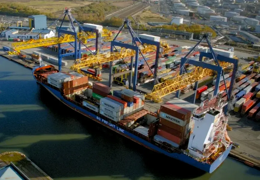 A container ship at a UK port with cranes loading cargo highlighting shipping delays.