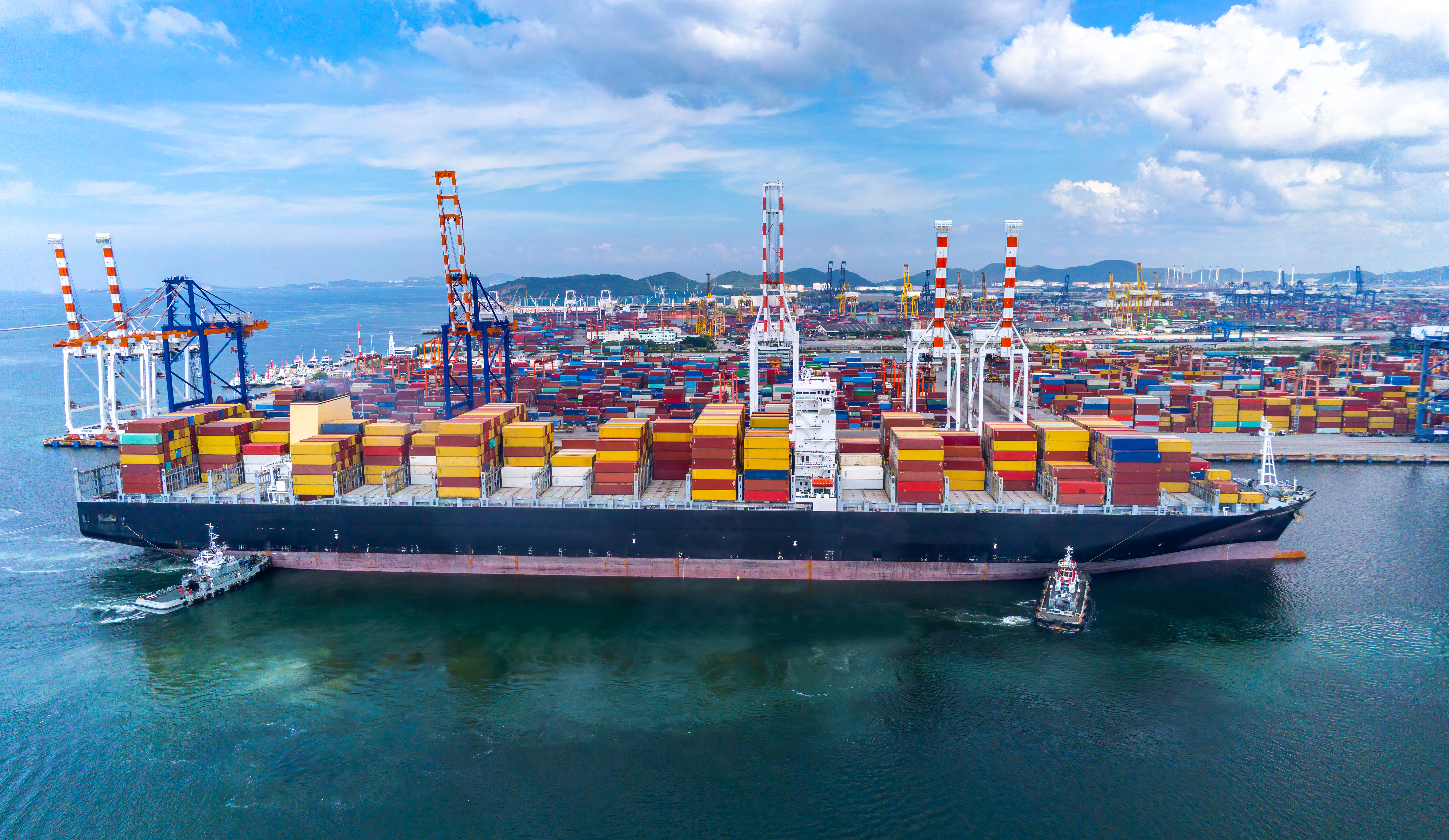 Aerial view of a large container ship loaded with colourful freight containers docking at a busy port, showing global logistics operations involved in managing supply chain risks.